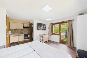 A compact room with a bed, a kitchenette, a dining area, and a window with curtains.