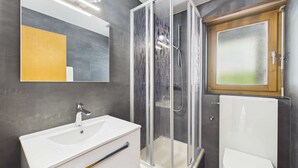 Un baño moderno con ducha de vidrio, lavamanos blanco y un espejo grande.