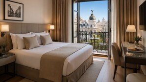A hotel room with a large bed, a desk with a chair, a balcony with a view of a cityscape, and a framed picture on the wall. - Hotel Mar Salada (Madrid)