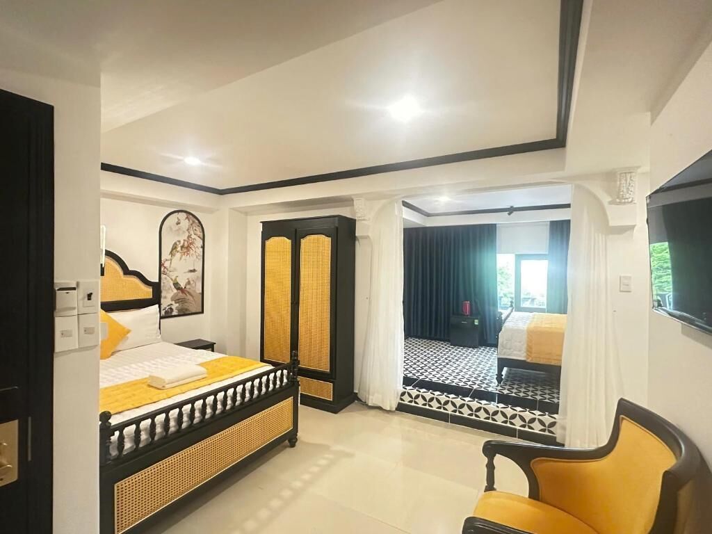Quarto com cama, uma cadeira, televisão e vista para outro espaço.