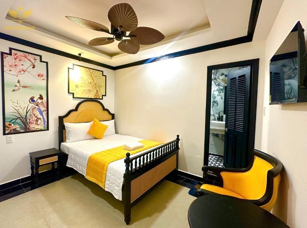 Quarto com cama, cadeira, mesa, ventoinha no teto e obras de arte nas paredes.
