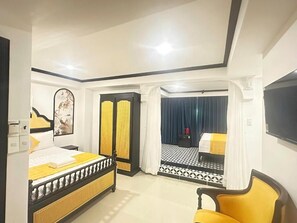 Quarto de hotel com cama, cadeira, televisão e varanda com piso estampado.