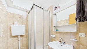 Un baño con inodoro, ducha, lavamanos y espejo.