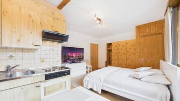 Een moderne keuken met houten kastjes, een ingebouwde magnetron en een spoelbak. Er is een bed met wit beddengoed en een poster van een stadsgezicht.