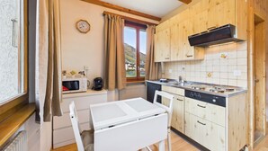 Una cocina con armarios de madera, microondas, estufa y ventana con cortinas.