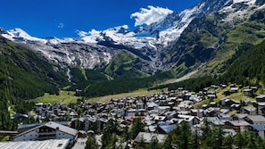 A mountain village with buildings clustered at the base, surrounded by snow-capped peaks and dense forests. - Panoramic View Studio Near Saas-Grund Cable Car (Saas-Grund)