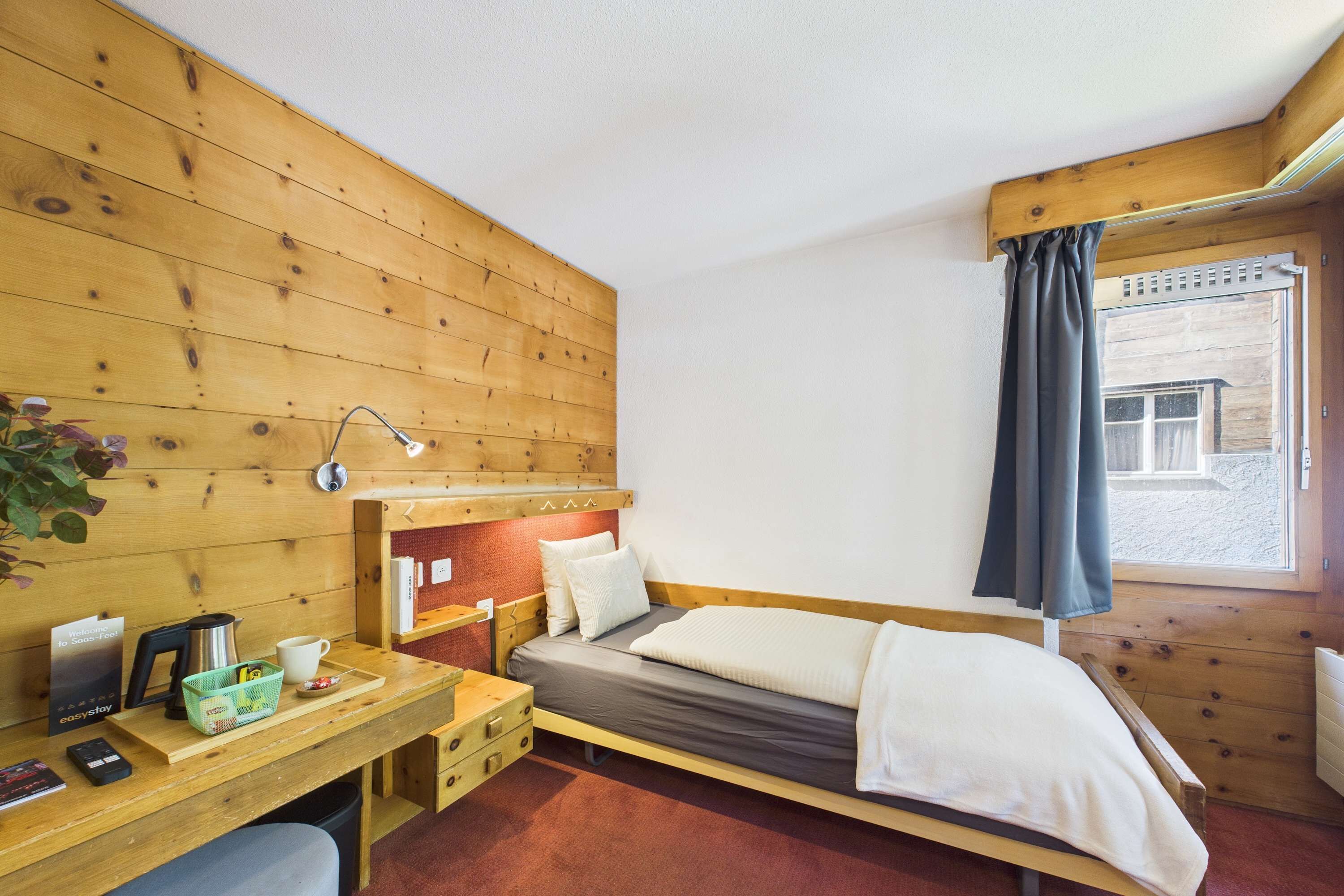 A wooden room with a bed, desk, and window.