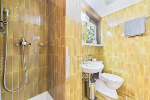 A bathroom with yellow tiles, a white sink, a toilet, and a shower with a handheld showerhead. - Central Studio with Mountain Views in Saas-Fee (Saas-Fee)