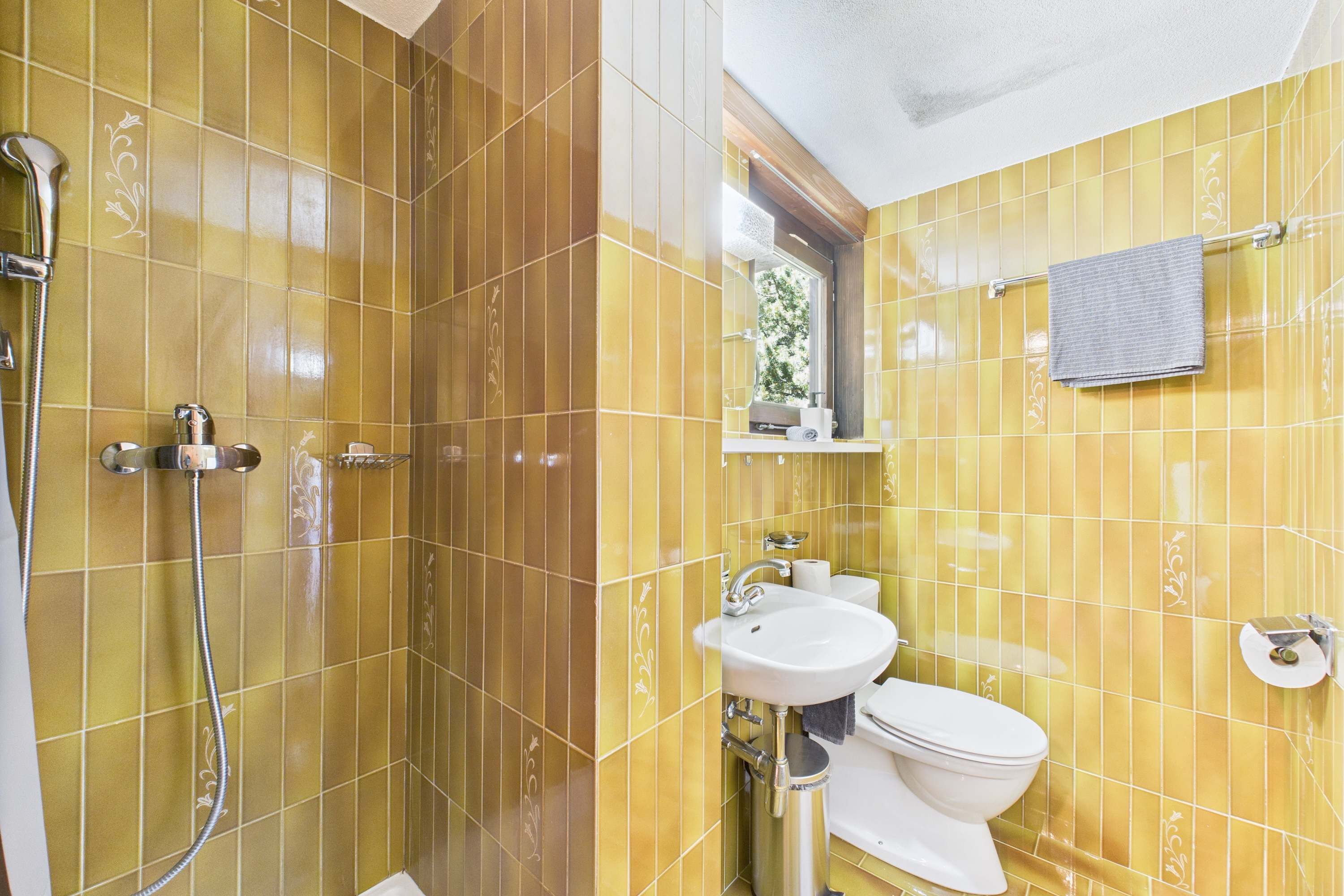 A bathroom with yellow tiles, a white sink, a toilet, and a shower.