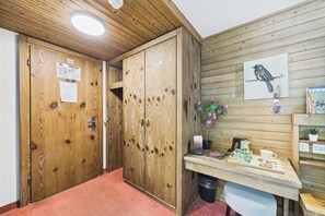 A wooden interior with a desk, a chair, a wall-mounted picture of a bird, and a trash bin. - Central Studio with Mountain Views in Saas-Fee (Saas-Fee)