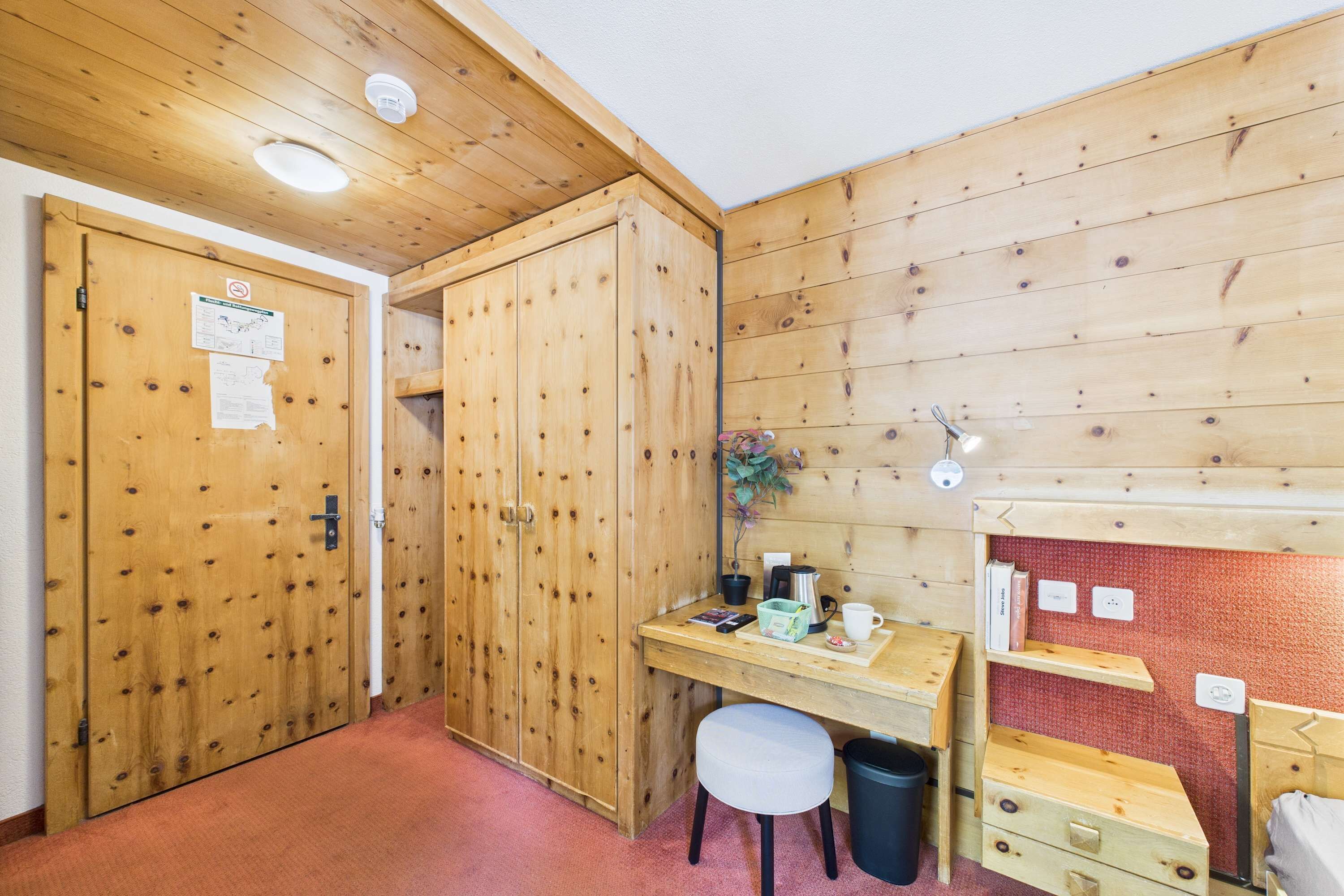 Une pièce aux murs lambrés, contenant un bureau, une chaise et un petit tabouret.