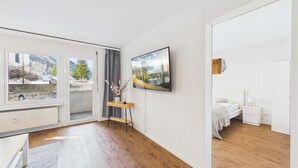 Quarto moderno com cama, mesa de cabeceira e televisão na parede.