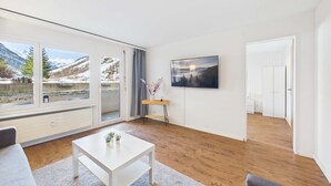 Uma sala de estar moderna com uma janela ampla, uma televisão de tela plana e piso de madeira.