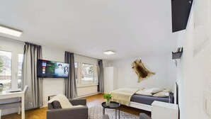 Ein modernes Zimmer mit Bett, Schreibtisch, Fernseher und Fenster.