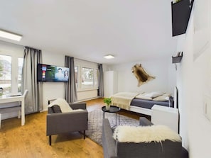 A modern room with a bed, a desk, a TV, and a window.