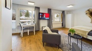 Ein modernes Hotelzimmer mit Bett, Schreibtisch, Stuhl, Fernseher und großen Fenstern.