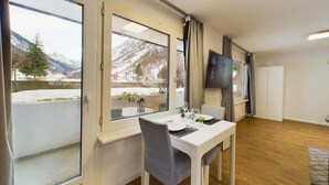 Ein Zimmer mit Esstisch, Stühlen, einem Fernseher und großen Fenstern mit Blick auf die Berge.
