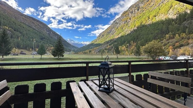 Una terraza de madera con bancos, un farol y vistas a un valle con montañas.