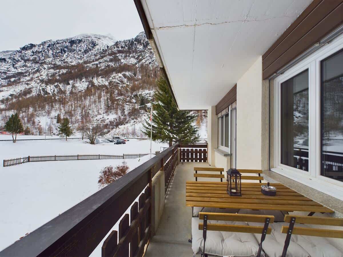 Un balcon avec une table et des bancs en bois, donnant sur un paysage enneigé avec des montagnes.