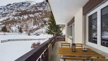 Un balcon avec une table et des bancs en bois, donnant sur un paysage enneigé avec des montagnes.