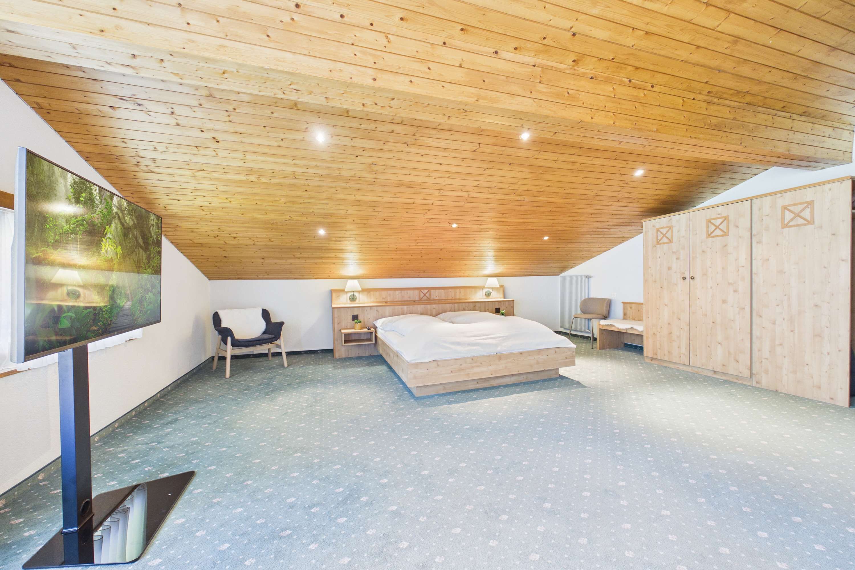 Ein Schlafzimmer mit Holzboden, einem Bett, einem Fernseher, einem Kleiderschrank und einem Sessel.