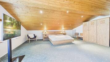 Ein Schlafzimmer mit Holzboden, einem Bett, einem Fernseher, einem Kleiderschrank und einem Sessel.