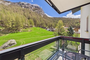 A balcony with a glass railing overlooking a mountainous landscape with green fields and houses.
