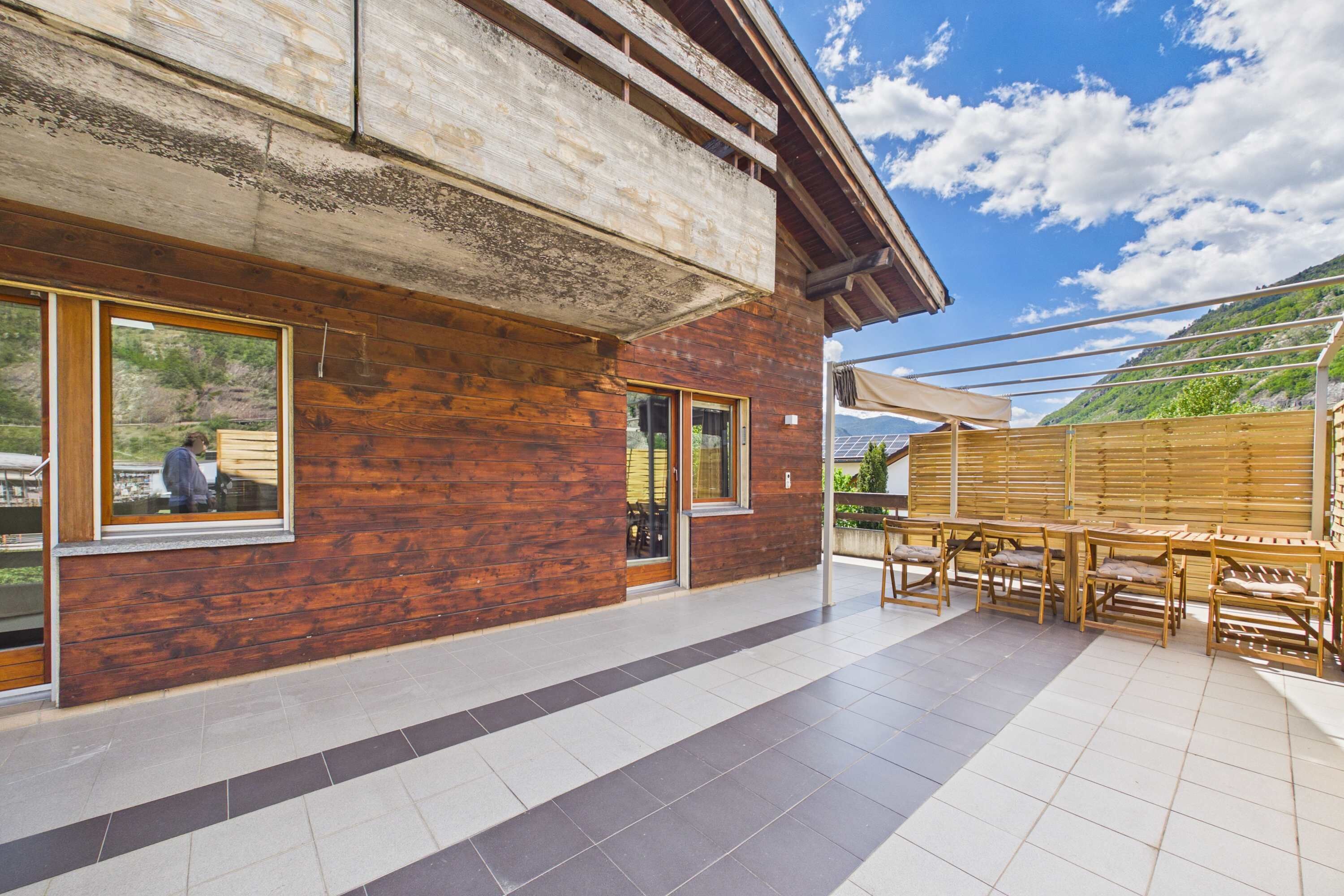 Un bâtiment en bois doté de grandes fenêtres, d’un espace extérieur aménagé pour s’asseoir et d’une terrasse carrelée.