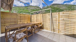 Un espacio de estar al aire libre con madera, que incluye una mesa, sillas, una sección cubierta y vistas a un paisaje montañoso.