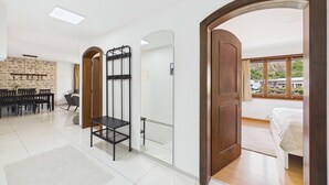 Una habitación de hotel moderna con una cama, un área de comedor con sillas, un espejo y una puerta de madera que da a otra habitación.