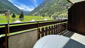 En balkon med udsigt over et bjerglandskab, et træværksgelænder og et bord.