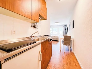 A compact kitchen with wooden cabinets, a built-in stove, and a dining area with a chair.