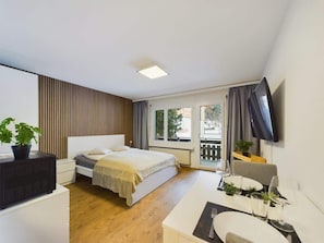 Een moderne hotelkamer met een bed, nachtkastje, televisie en een balkon met uitzicht.