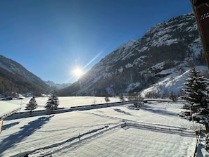 Een besneeerd landschap met bergen, een heldere lucht en een schijnende zon.