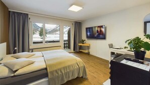 Et hotelværelse med en seng, et skrivebord, et fjernsyn og et vindue med udsigt over et sneklædt landskab.