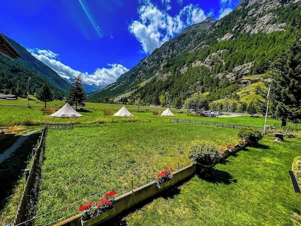 Un paysage montagneux avec des champs verdoyants, des tentes blanches et un ciel dégagé.
