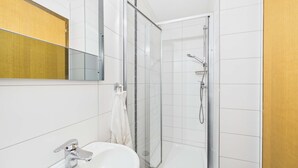 A bathroom with a white sink, a glass shower enclosure, and a mirror. - Charming Studio with Mountain Views in Brig (Gamsen)