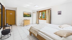 A hotel room with a bed, a desk, a chair, a TV, and a window with curtains. - Charming Studio with Mountain Views in Brig (Gamsen)
