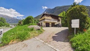 A two-story house with a garage, a paved driveway, and a mountain backdrop. - Charming Studio with Mountain Views in Brig (Gamsen)