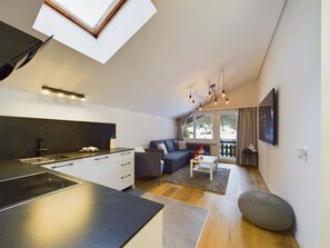 Una cocina moderna con estufa integrada, un comedor con mesa y sillas, un sofá y un televisor montado en la pared.