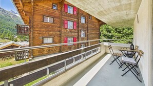 Un chalet de madera con balcones, una terraza con sillas y un paisaje de montañas al fondo.