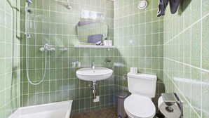 Un baño con baldosas verdes con diseño, un lavabo blanco, un inodoro, una ducha y un espejo.