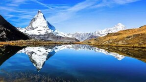 A mountain reflected in a calm lake with snow-capped peaks. - Mountain View Apartment Steps from Zermatt (Täsch)