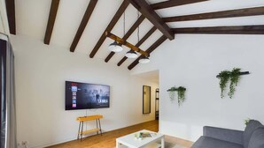 A living room with a TV, sofa, coffee table, wooden floor, and ceiling beams. - Mountain View Apartment Steps from Zermatt (Täsch)