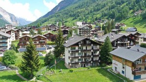 Un pueblo de montaña con edificios de varios pisos, algunos con balcones, rodeado de exuberante vegetación y montañas.