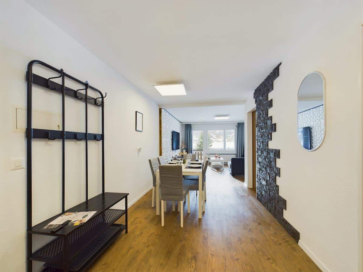 A room with a dining table, chairs, a black metal rack, and a stone wall.