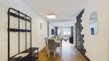 A room with a dining table, chairs, a black metal rack, and a stone wall.