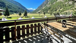 Un balcón con vistas a un paisaje montañoso, una mesa de madera y una silla.