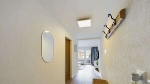 Een hal met een houten bankje, een ronde spiegel en een wandlamp.
