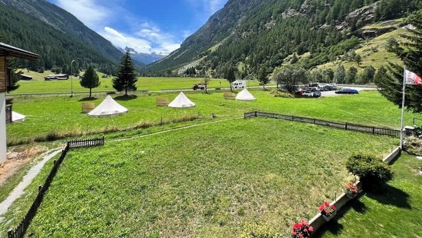 Een bergachtig landschap met tenten en een gebouw, wat wijst op een camping of buitenaankommodatie.